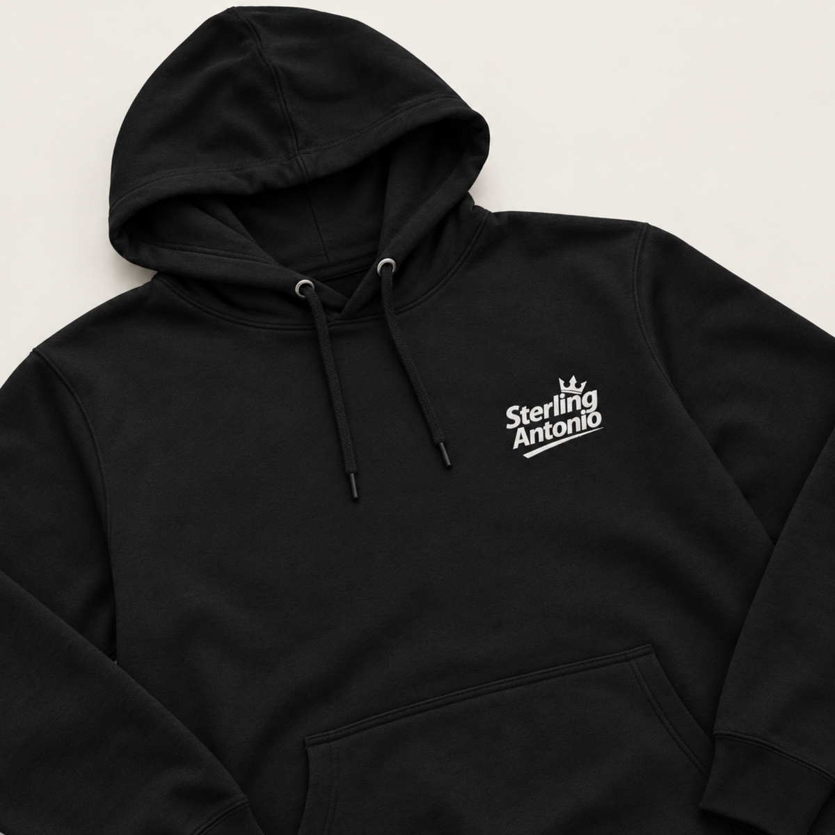 A black pullover hoodie with a white 'Sterling Antonio' graphic printed on the left chest, displayed on a light beige background.