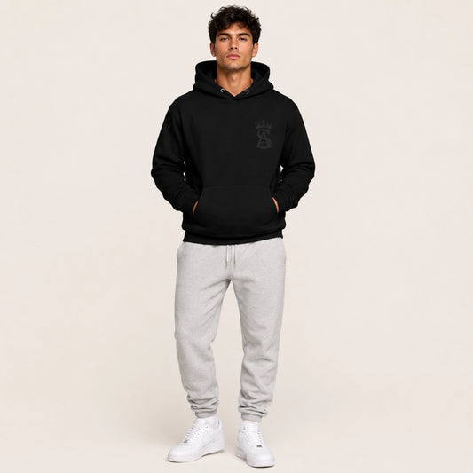 Man wearing a black hoodie with a logo and gray sweatpants on a beige background