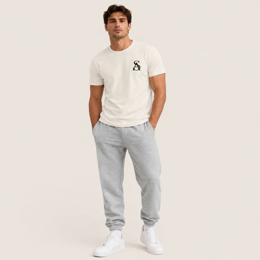 Man wearing a white t-shirt with a logo and gray sweatpants on a light background