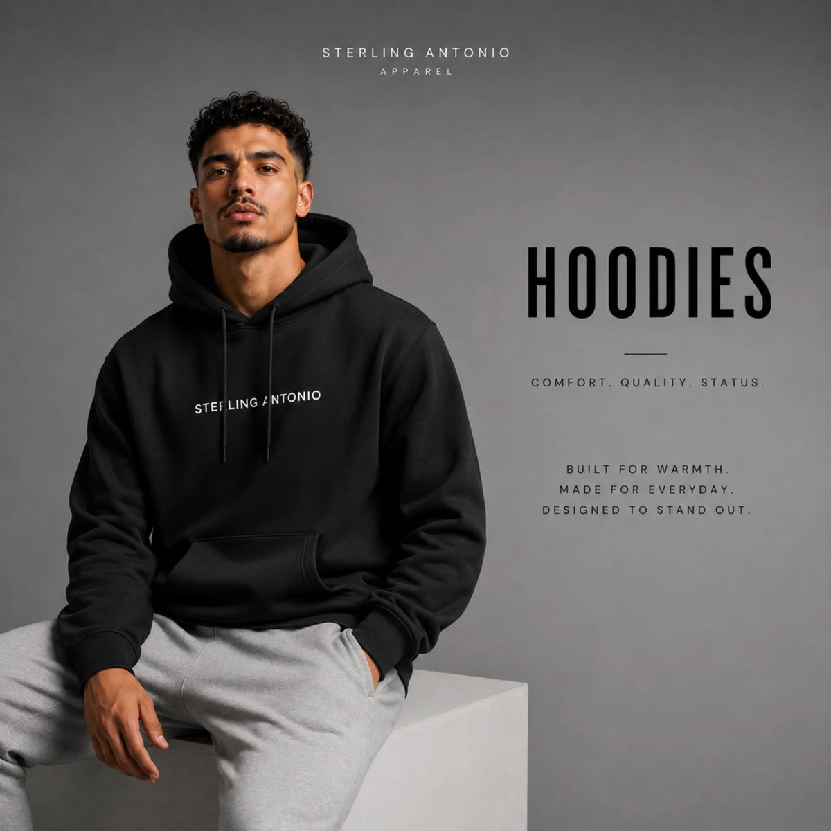 Male model wearing a black Sterling Antonio premium hoodie with gray sweatpants in a modern studio, showcasing the Sterling Antonio Hoodies collection of luxury streetwear.