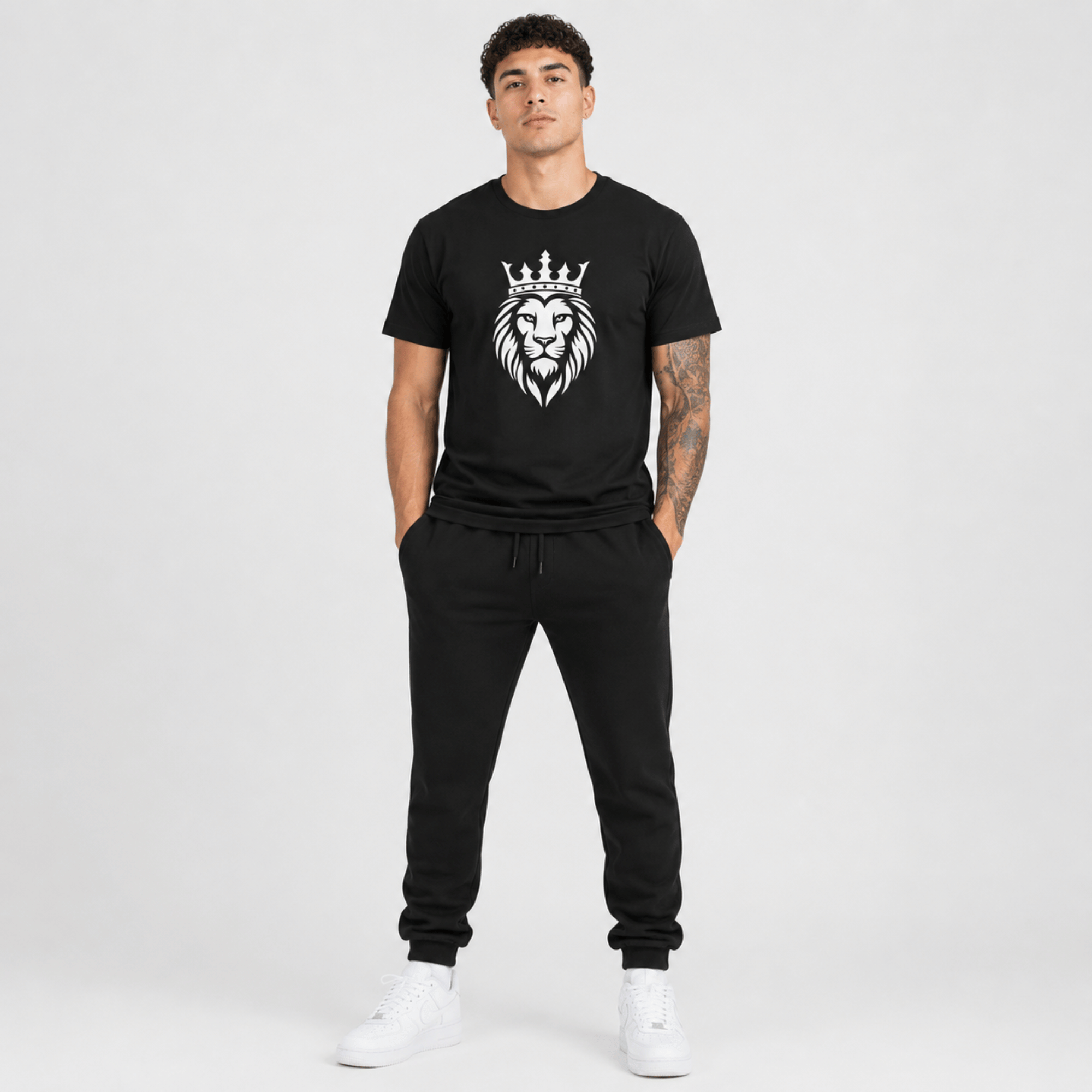 Male fashion model wearing a black t-shirt featuring a white crowned lion graphic with matching black sweatpants and white sneakers.