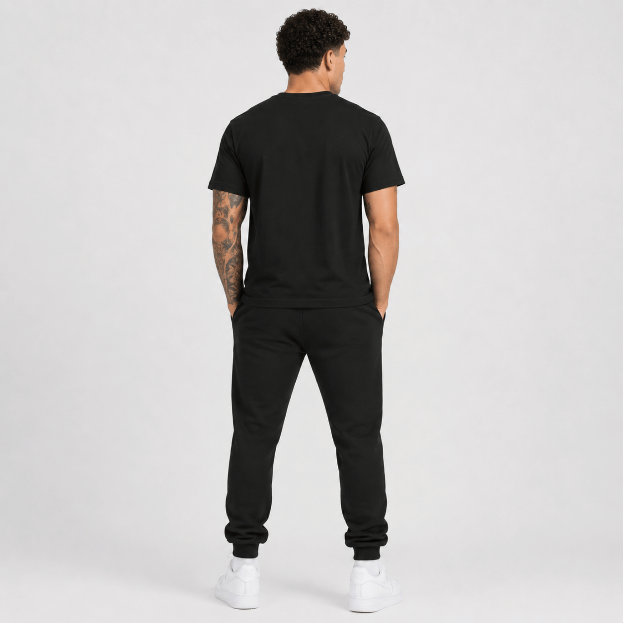 Rear view of a male fashion model wearing a black Sterling Antonio cotton jersey t-shirt with matching black sweatpants and white sneakers