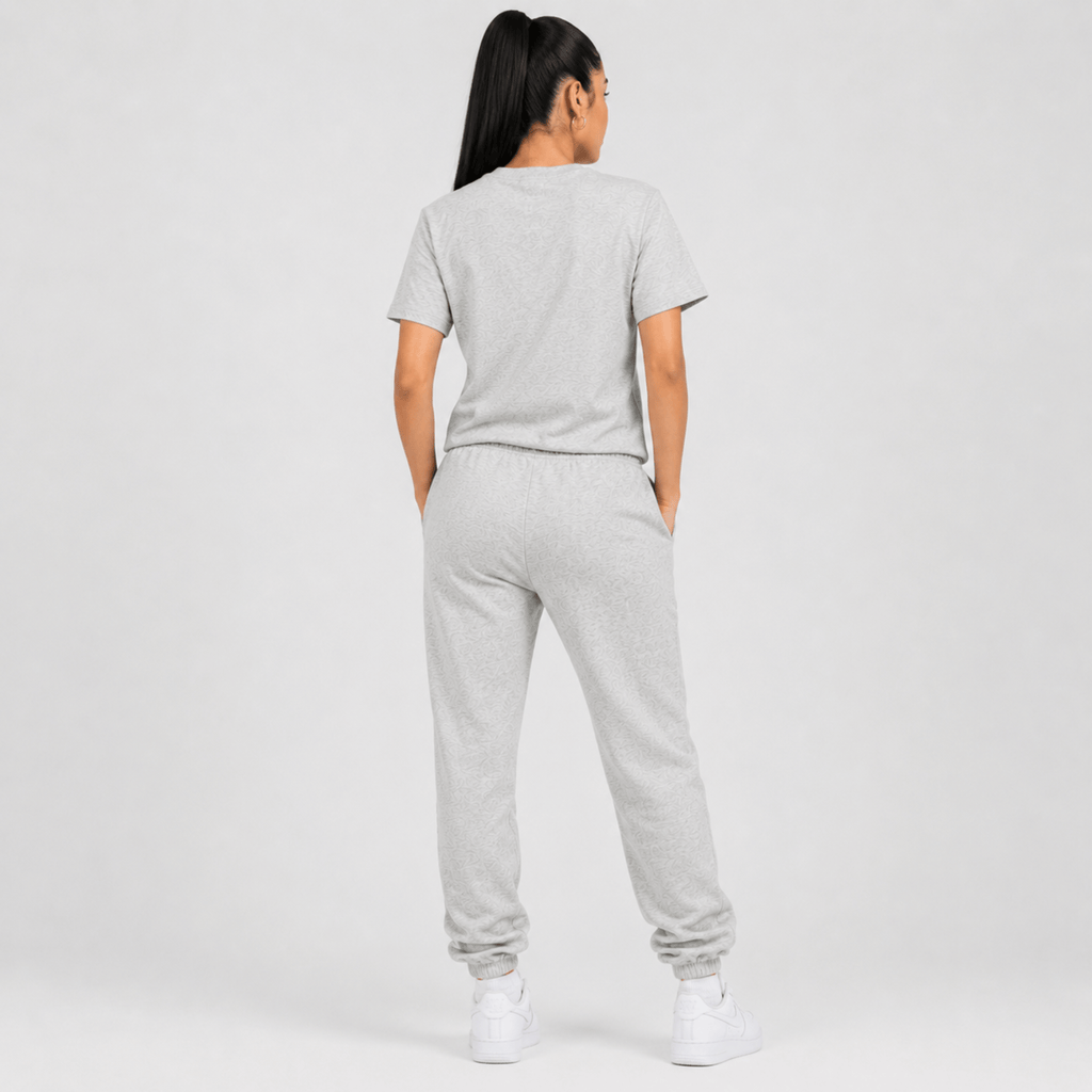 Rear view of a female fashion model wearing a heather grey Sterling Antonio cotton jersey t-shirt with matching sweatpants and white sneakers on a light grey background.