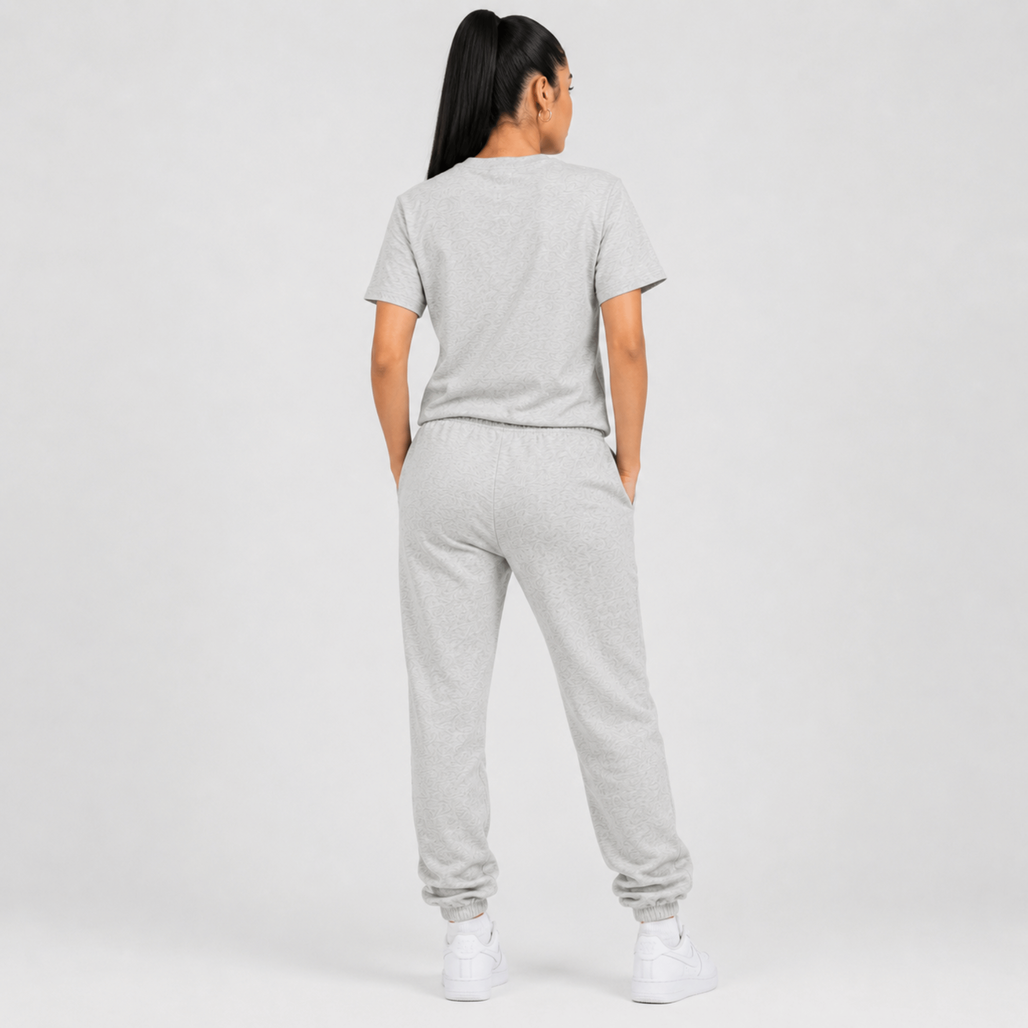 Rear view of a female fashion model wearing a heather grey Sterling Antonio cotton jersey t-shirt with matching sweatpants and white sneakers on a light grey background.