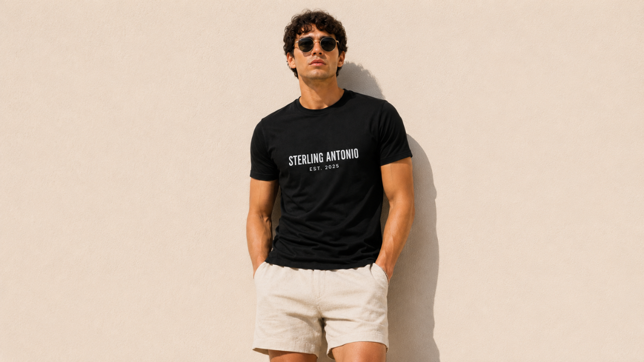 Man wearing a black t-shirt with 'STERLING ANTONIO' text, sunglasses, and white shorts against a beige background