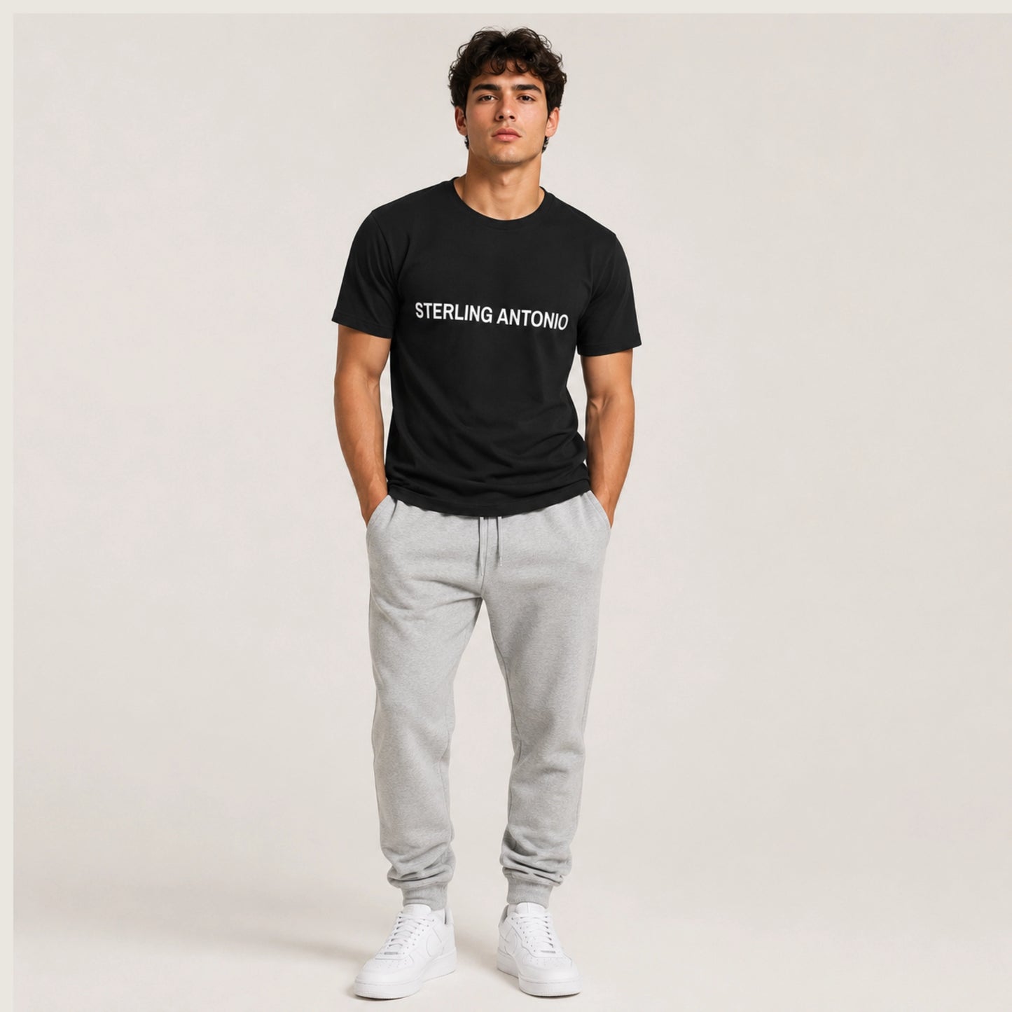 Man wearing a black t-shirt with 'STERLING ANTONIO' text, gray sweatpants, and white sneakers on a plain background