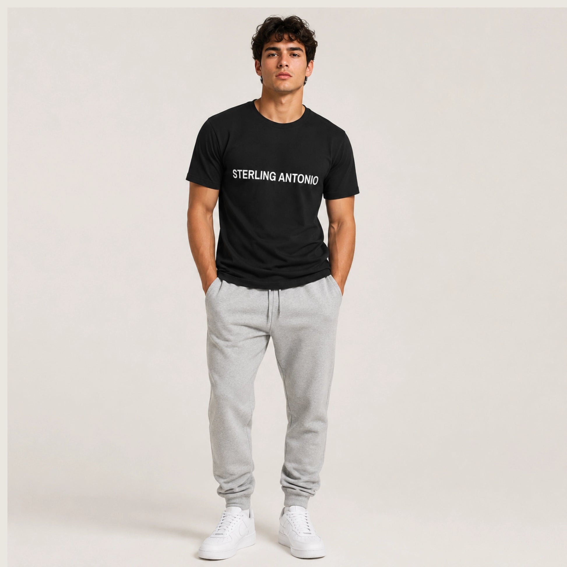 Man wearing a black t-shirt with 'STERLING ANTONIO' text, gray sweatpants, and white sneakers on a plain background