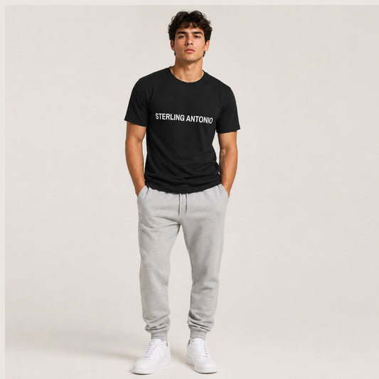 Man wearing a black t-shirt with 'STERLING ANTONIO' text, gray sweatpants, and white sneakers on a plain background