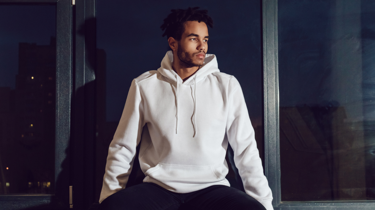 Man wearing a white hoodie sitting on a bench at night.