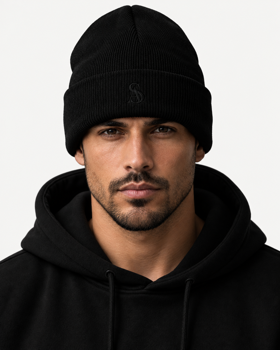 The Black Label Beanie on model. Black cuffed knit beanie with a tonal SA monogram on the cuff, worn with a black hoodie.