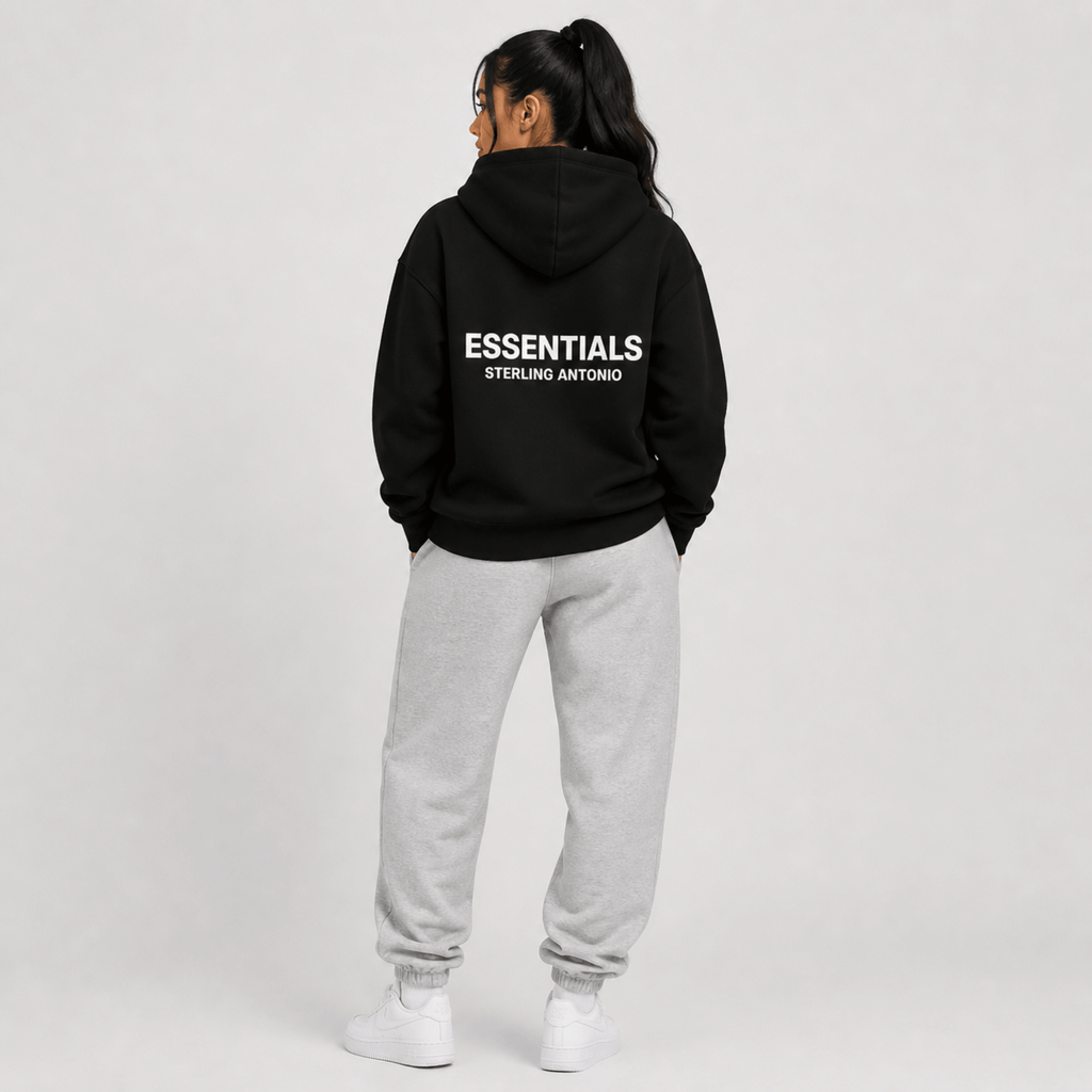 Person wearing a black hoodie with 'ESSENTIALS' branding on the back, standing against a plain background.