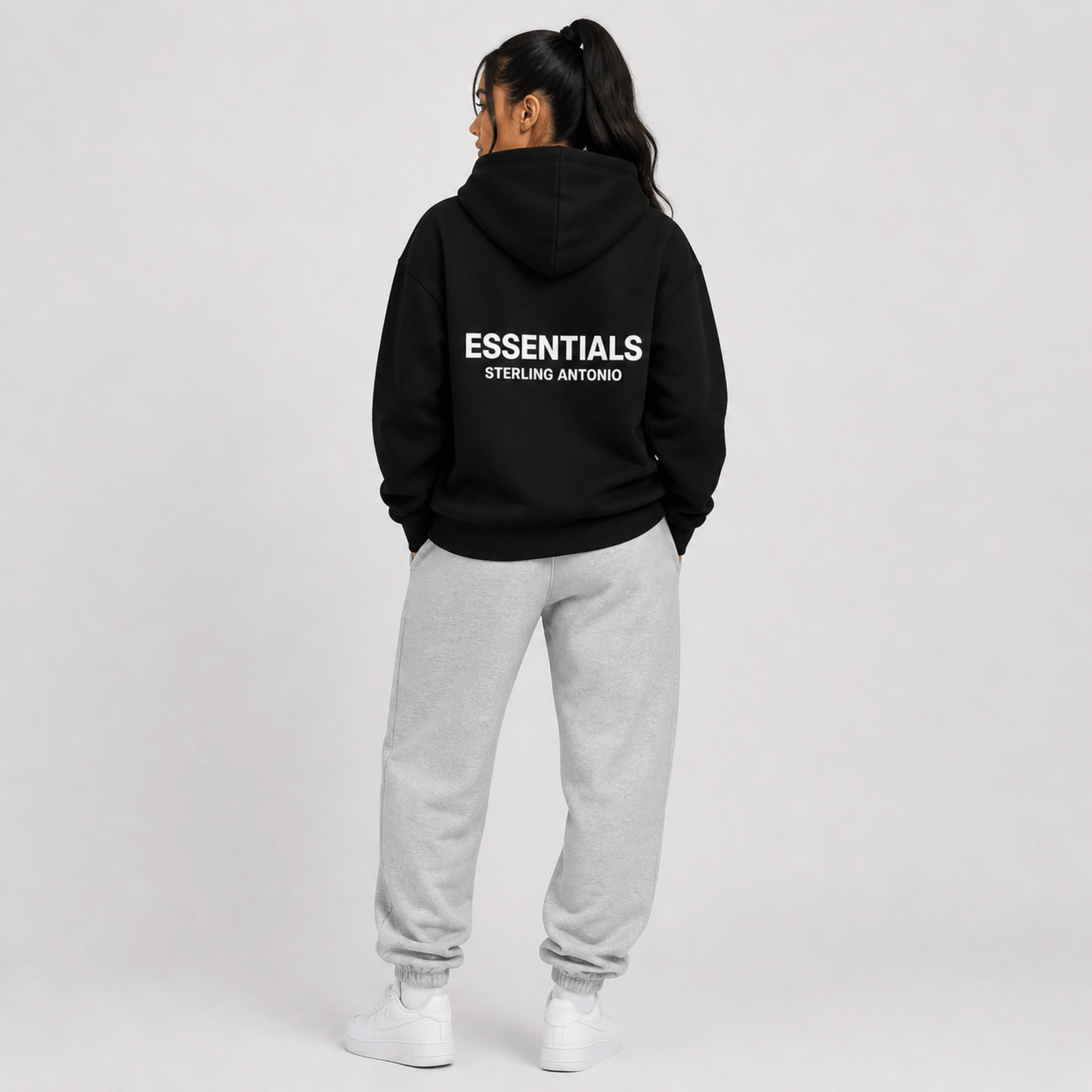Person wearing a black hoodie with 'ESSENTIALS' branding on the back, standing against a plain background.