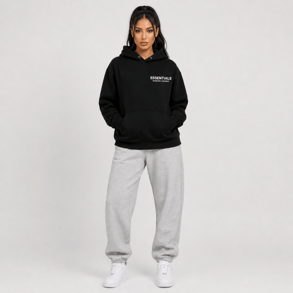 Person wearing a black hoodie with 'ESSENTIALS' text and gray sweatpants on a white background