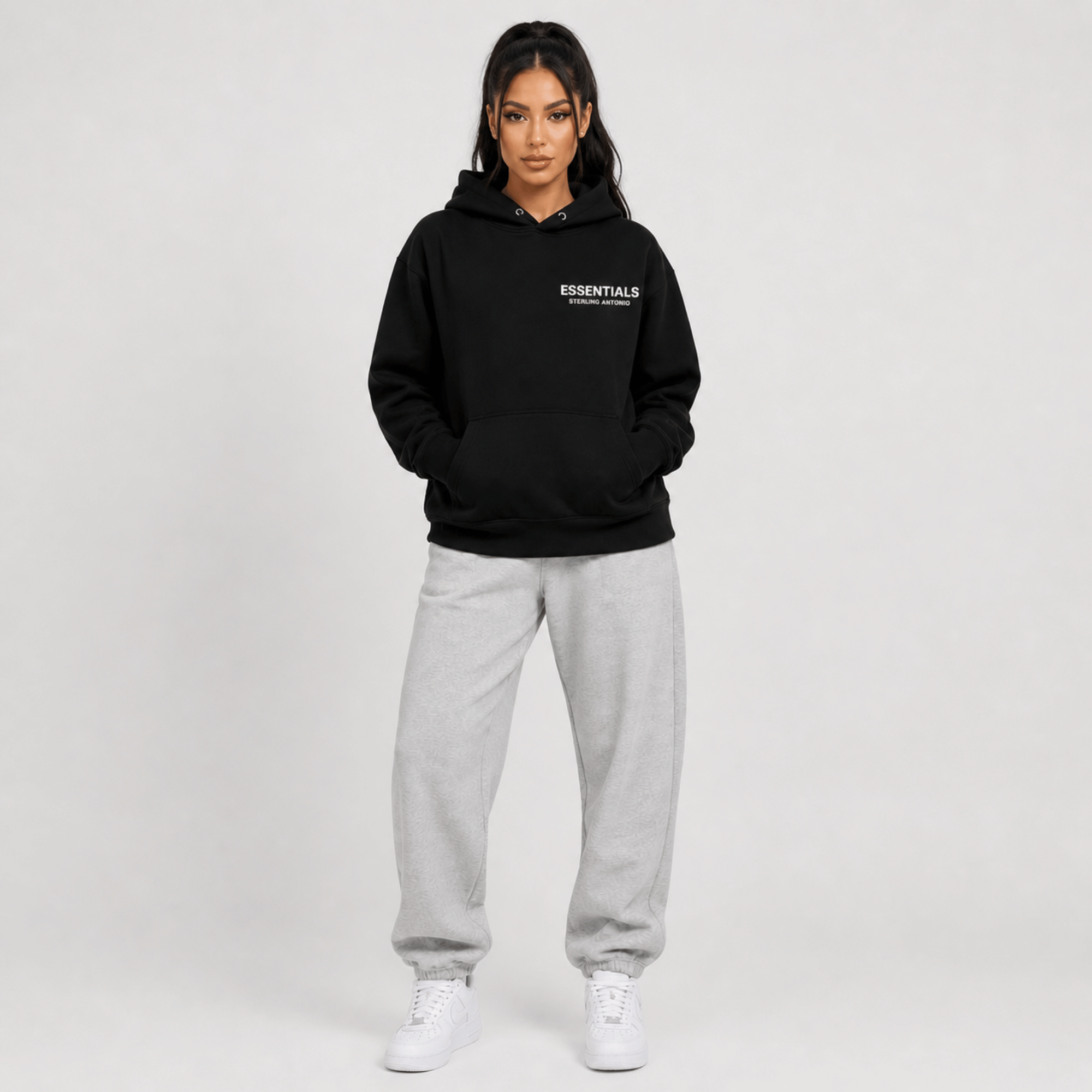 Person wearing a black hoodie with 'ESSENTIALS' text and gray sweatpants on a white background
