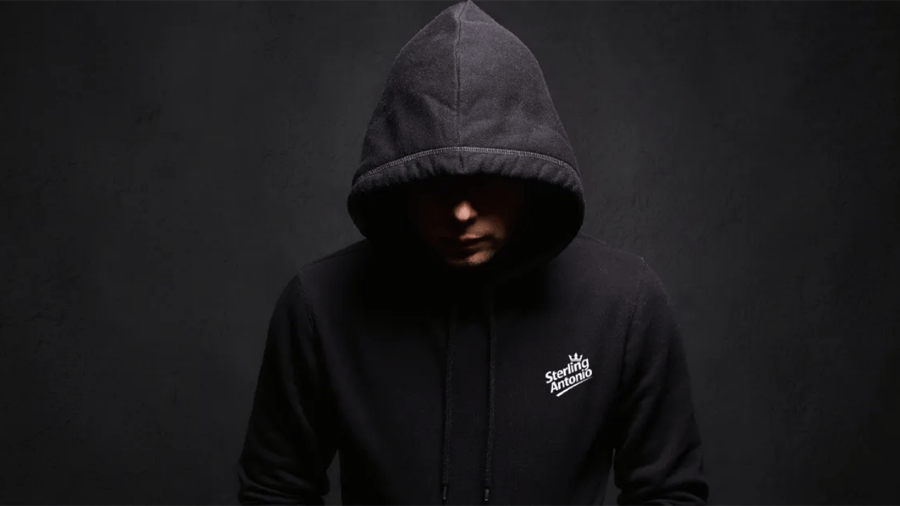 Person wearing a black hoodie with a logo on a dark background