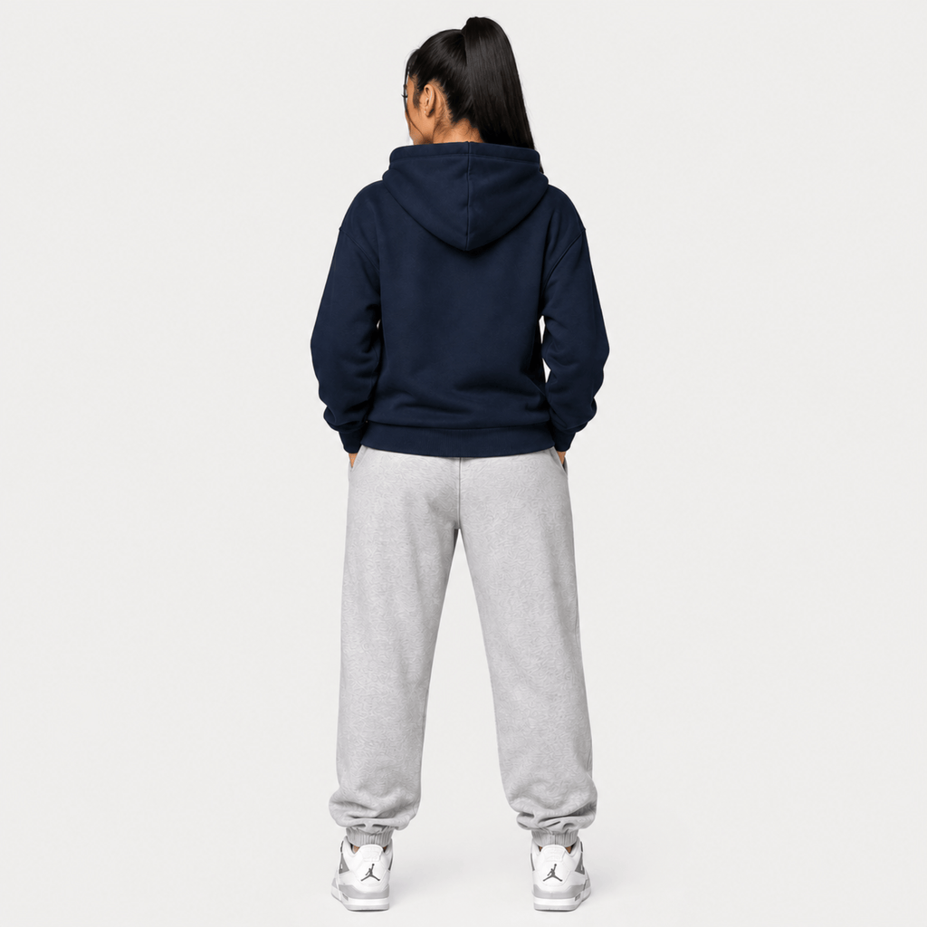Person wearing a navy hoodie with a lion emblem on a light grey background rear view