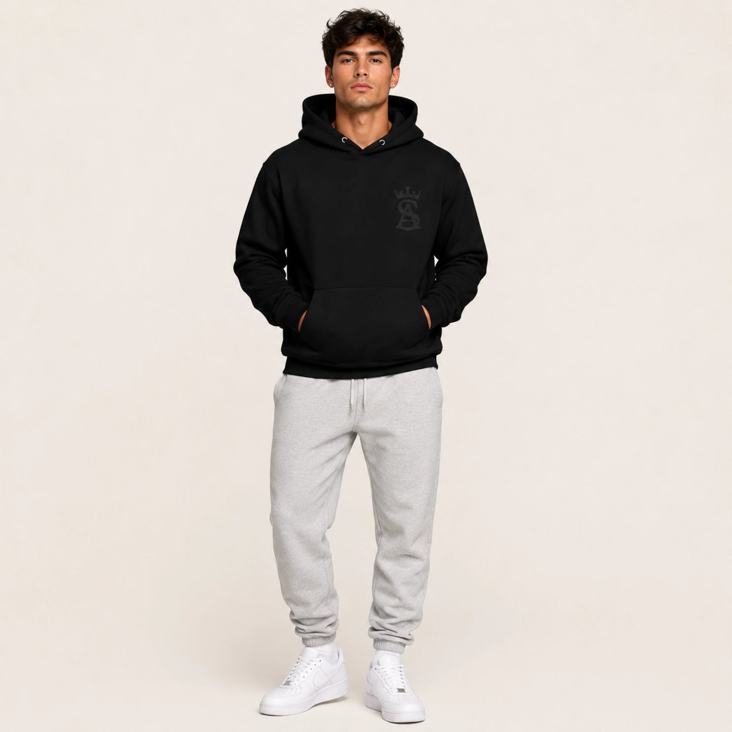 Man wearing a black hoodie with a logo and gray sweatpants on a beige background