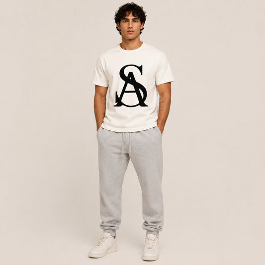 Person wearing a white t-shirt with a logo and gray pants on a plain background