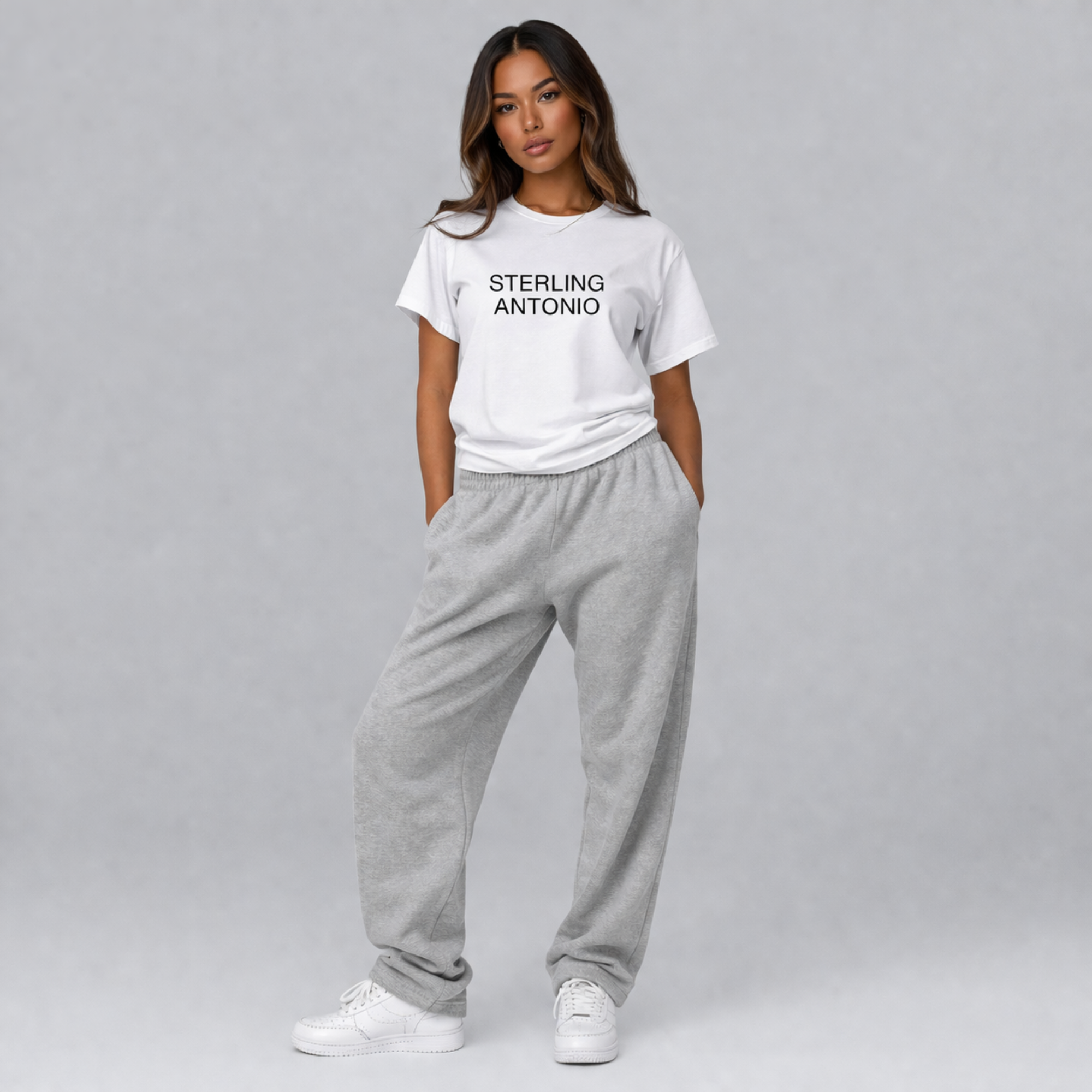 Woman wearing a white t-shirt with 'STERLING ANTONIO' text and gray sweatpants on a gray background