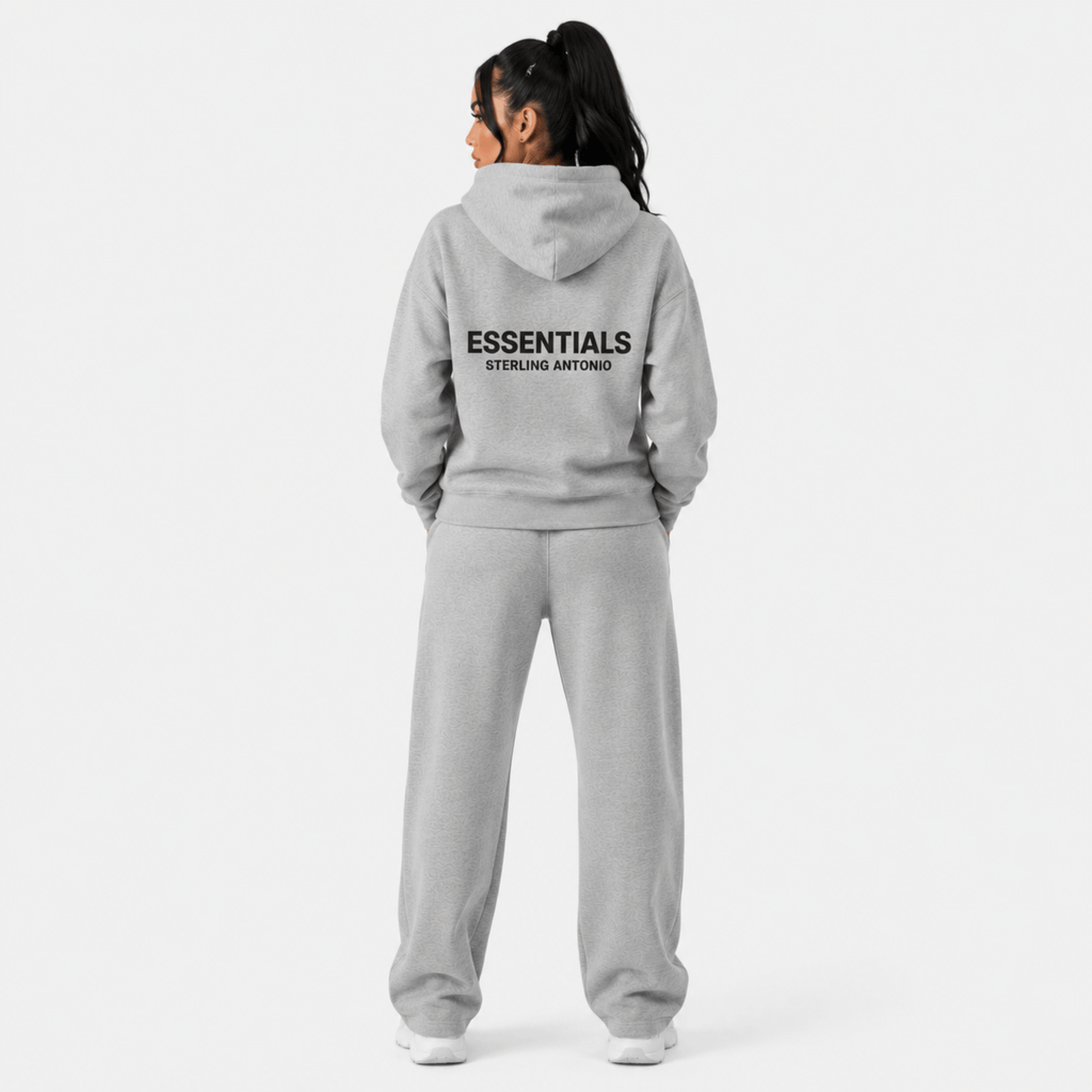 Rear view of female model wearing Sterling Antonio carbon grey essentials hoodie and matching sweatpants with oversized back logo print on light grey background