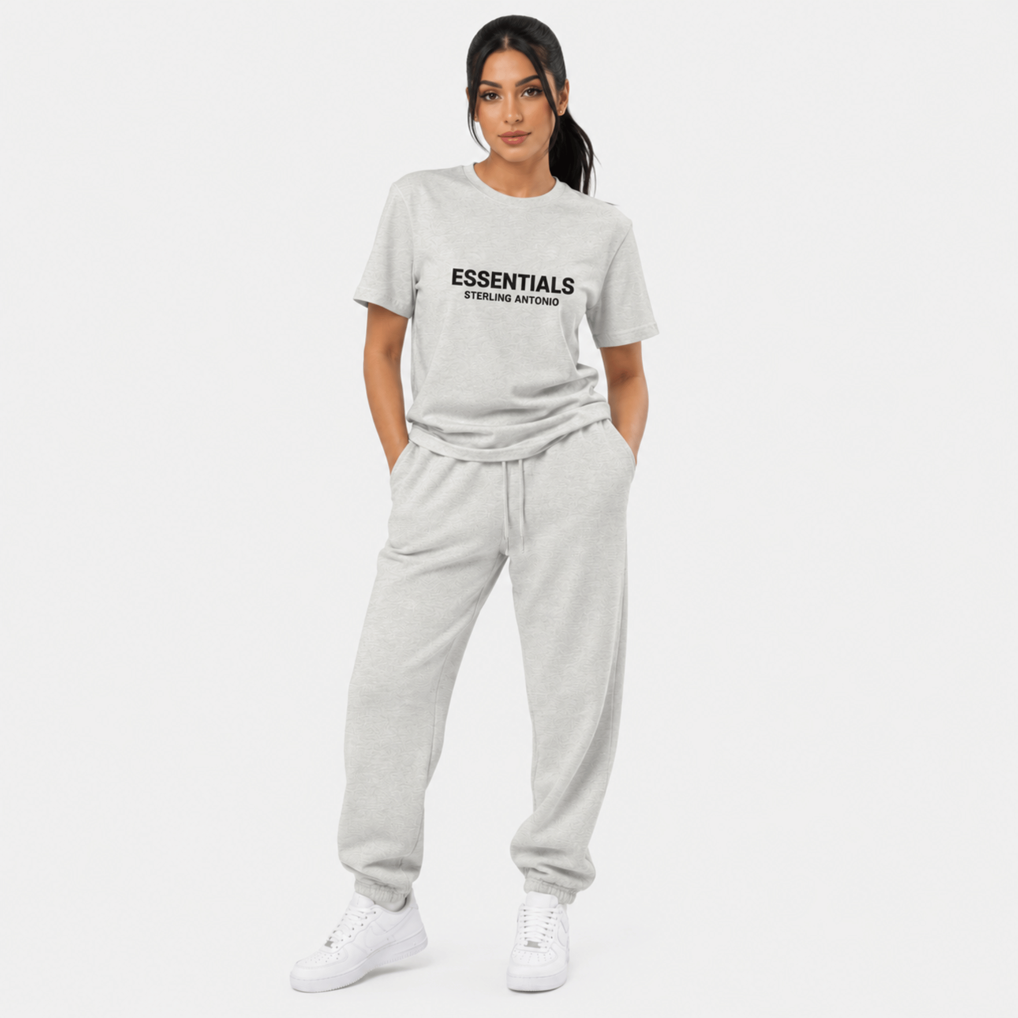 Female model wearing grey Essentials Sterling Antonio t-shirt with matching sweatpants and white sneakers against light grey background