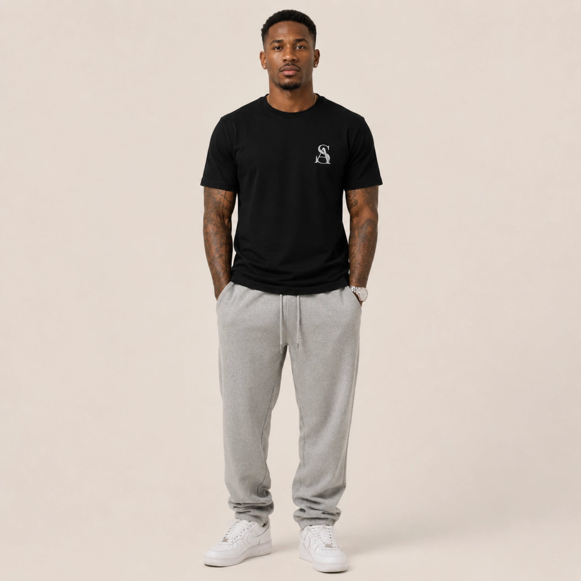 Man wearing a black t-shirt with a logo and gray sweatpants on a beige background