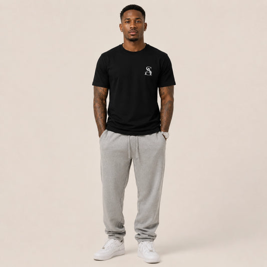 Man wearing a black t-shirt with a logo and gray sweatpants on a beige background