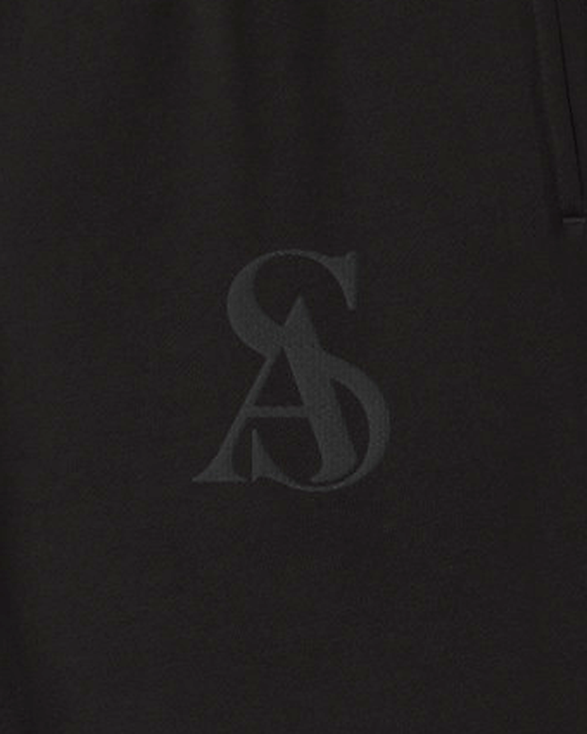 Close-up of the tonal SA monogram embroidered black on black at the left thigh of The Black Label Sweatpant. Sterling Antonio