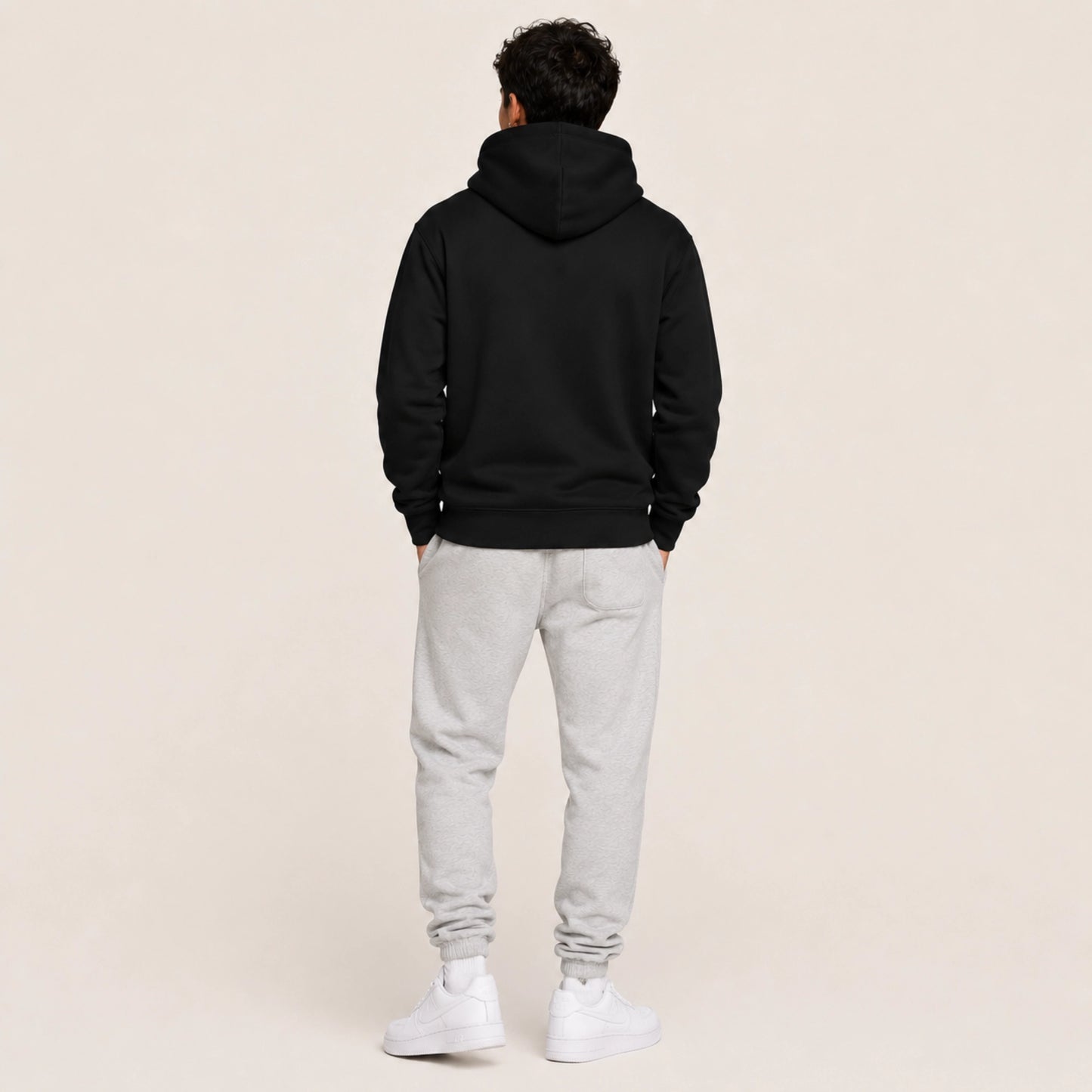 Person wearing a black hoodie and gray sweatpants on a beige background