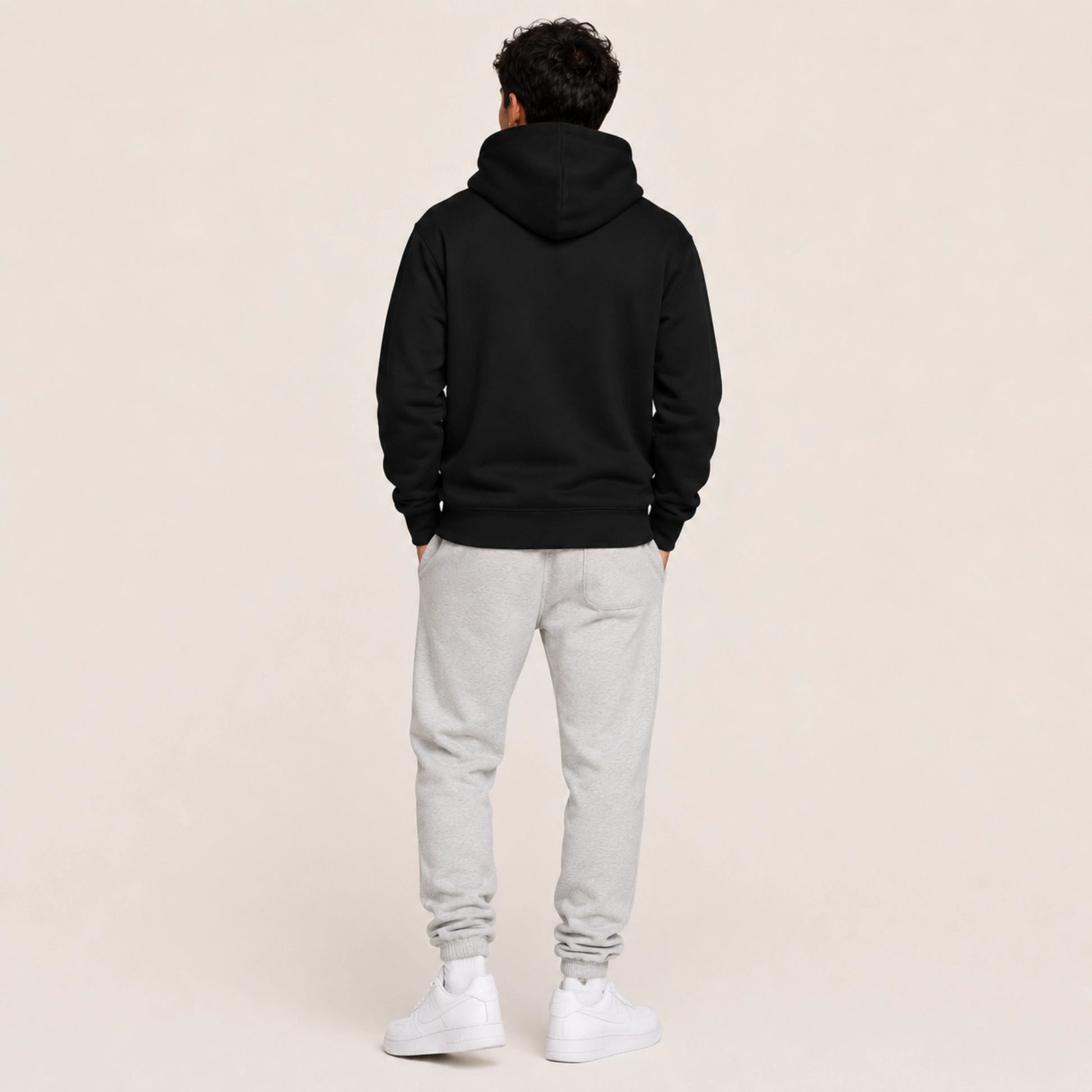 Person wearing a black hoodie and gray sweatpants on a beige background