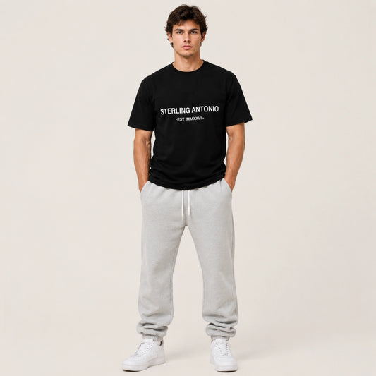 Man wearing a black t-shirt with text and gray pants on a plain background
